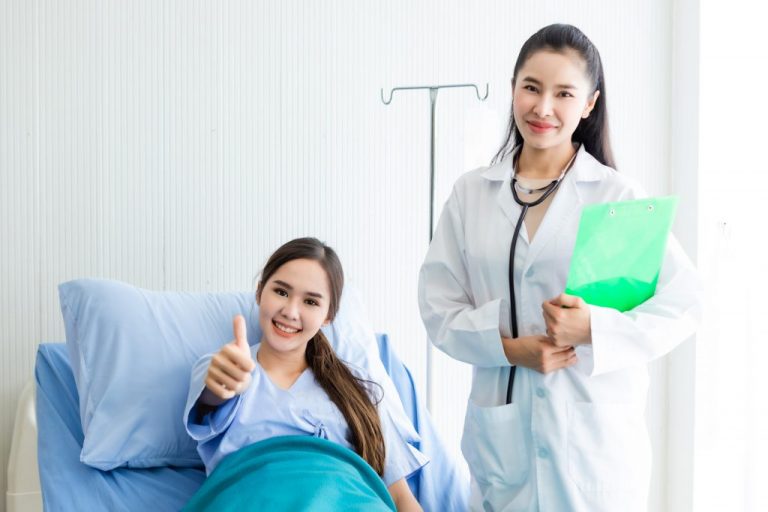 Asian young female patient on bed showing thumbs up with smiley face very good symptom to asian young female doctor in hospital background.