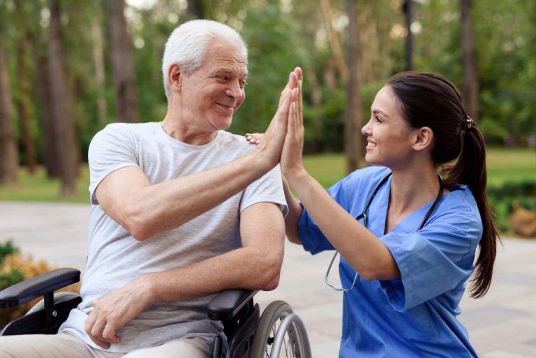 A nurse and an old man in a wheelchair high five.